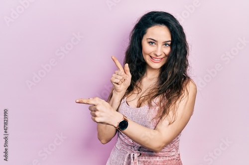 Young hispanic woman wearing casual clothes smiling and looking at the camera pointing with two hands and fingers to the side. © Krakenimages.com