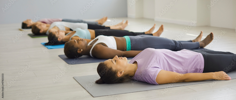 Toned sporty millennial diverse girls group lying on mat meditate practice yoga pilates. Calm active fit young multiracial women group train workout exercise together. Health, meditation concept. - obrazy, fototapety, plakaty 