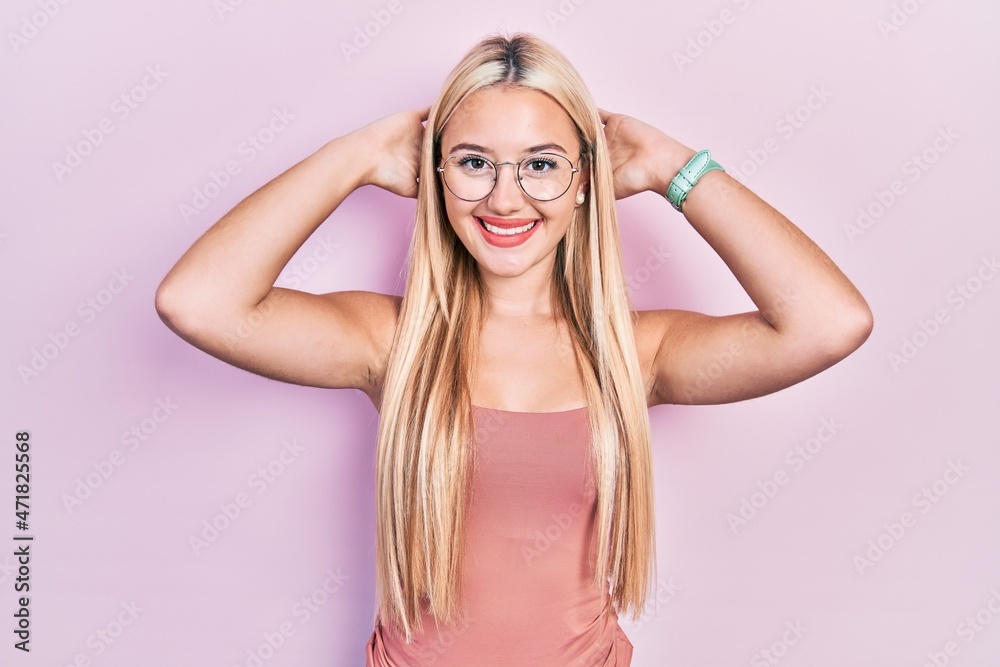 Young blonde girl wearing casual clothes relaxing and stretching, arms and hands behind head and neck smiling happy