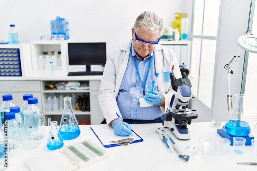 Middle age grey-haired man wearing scientist uniform holding test tube and write on document at laboratory Middle age grey-haired man wearing scientist uniform holding test tube and write on document at laboratory