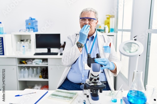 Senior caucasian man working at scientist laboratory laughing and embarrassed giggle covering mouth with hands, gossip and scandal concept