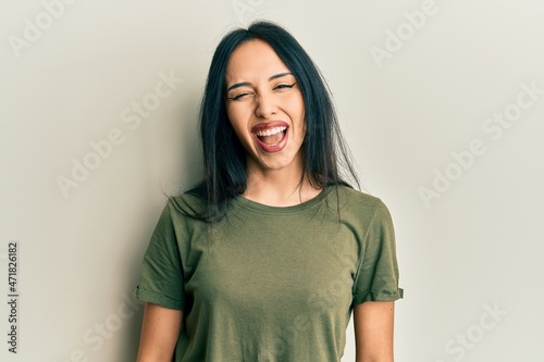 Young hispanic girl wearing casual t shirt winking looking at the camera with sexy expression, cheerful and happy face.