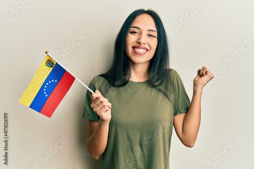 Young hispanic girl holding venezuelan flag screaming proud  celebrating victory and success very excited with raised arm