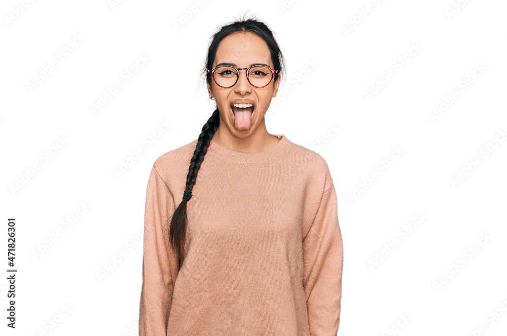 Young hispanic girl wearing casual clothes and glasses sticking tongue out happy with funny expression. emotion concept.