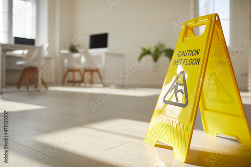 Yellow caution sign saying wet floor prevent people from falling on surface. Warning of slippery area for client or customer safety. Housekeeping, janitor concept. Maintenance and cleanup. photo