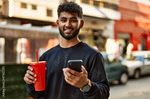 Young arab man using smartphone drinking soda at street