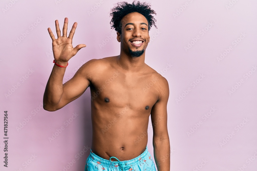 Fototapeta premium Young african american man with beard wearing swimsuit showing and pointing up with fingers number five while smiling confident and happy.