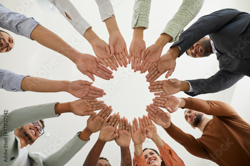 Group of happy diverse people joining hands. Mixed race team of different smiling young people putting hands together, cropped shot from below. Teamwork, community, help, support, volunteering concept photo