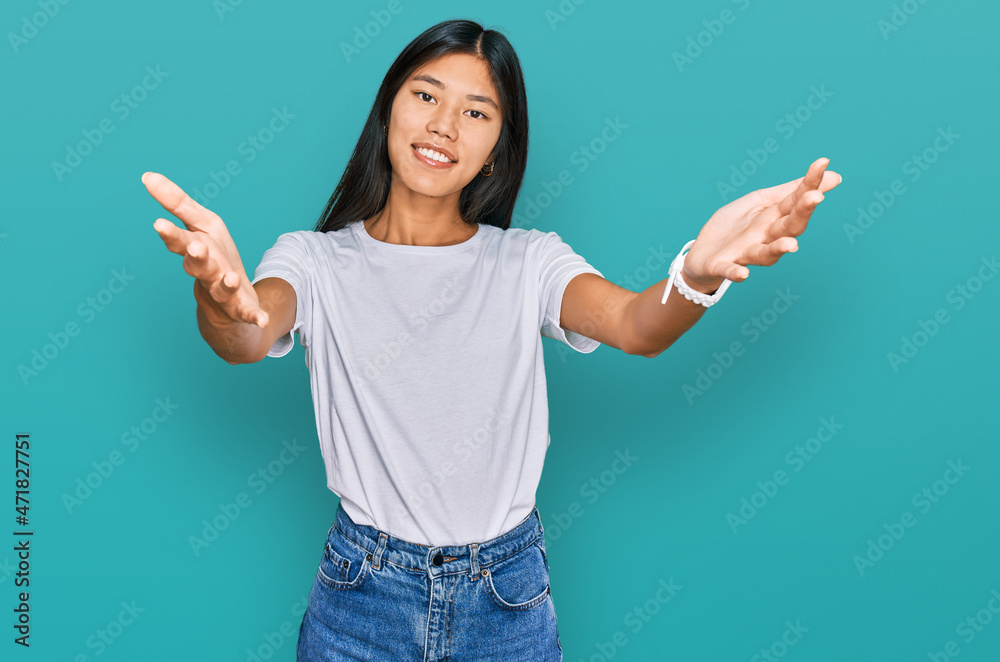 Beautiful young asian woman wearing casual white t shirt looking at the camera smiling with open arms for hug. cheerful expression embracing happiness. Beautiful young asian woman wearing casual white t shirt looking at the camera smiling with open arms for hug. cheerful expression embracing happiness.