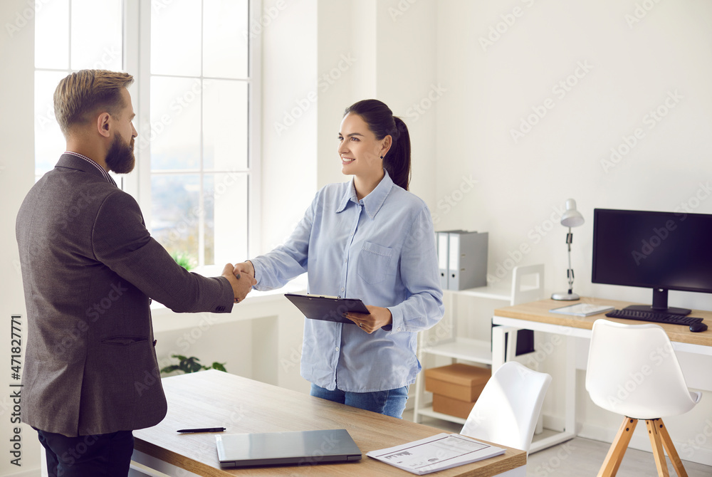 Thank you for choosing our service. Two happy young people shaking hands after business meeting. Friendly polite female bank manager holding clipboard and welcoming client in office Thank you for choosing our service. Two happy young people shaking hands after business meeting. Friendly polite female bank manager holding clipboard and welcoming client in office
