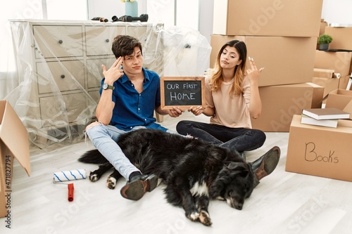 Photography Young caucasian couple with dog holding our first home blackboard at new house shooting and killing oneself pointing hand and fingers to head like gun, suicide gesture