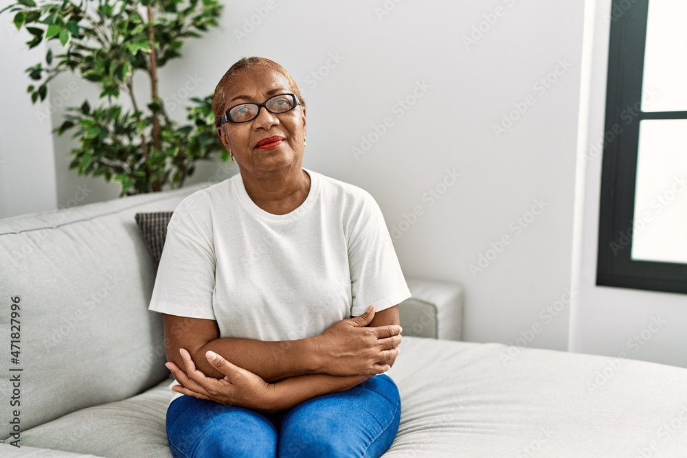 Mature hispanic woman sitting on the sofa at home skeptic and nervous, disapproving expression on face with crossed arms. negative person.
