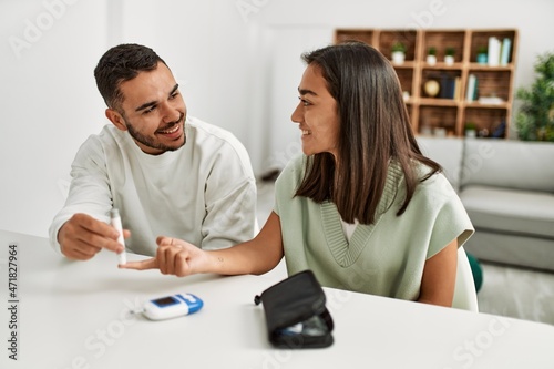 Young latin couple smiling happy measuring glucose at home.