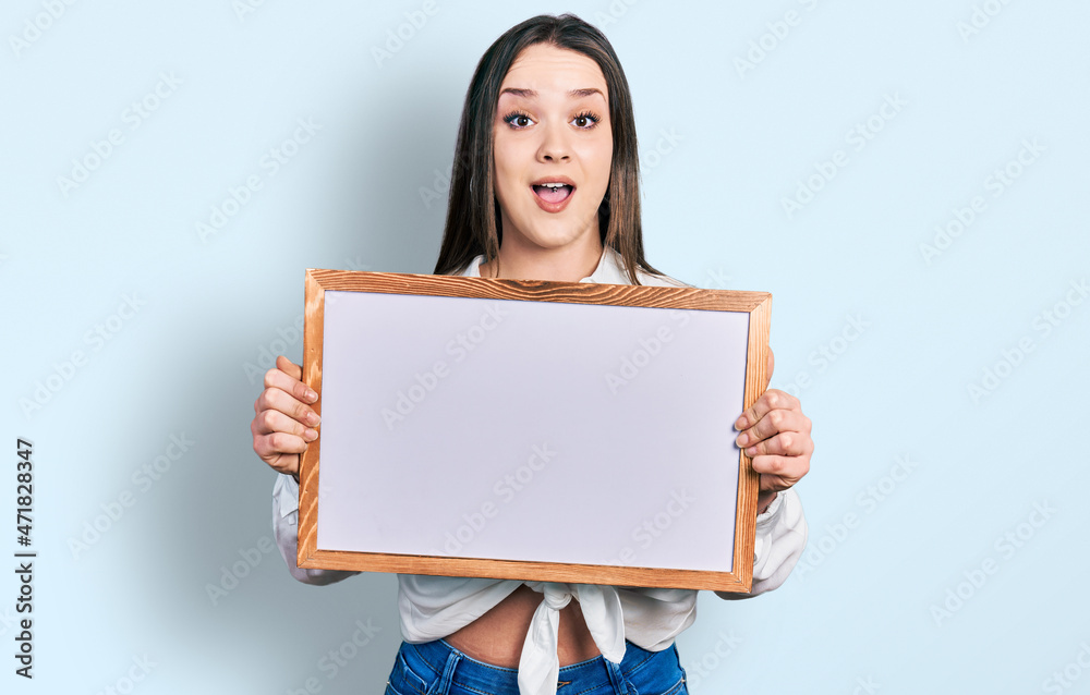 Young hispanic woman holding empty white chalkboard celebrating crazy and amazed for success with open eyes screaming excited. Young hispanic woman holding empty white chalkboard celebrating crazy and amazed for success with open eyes screaming excited.