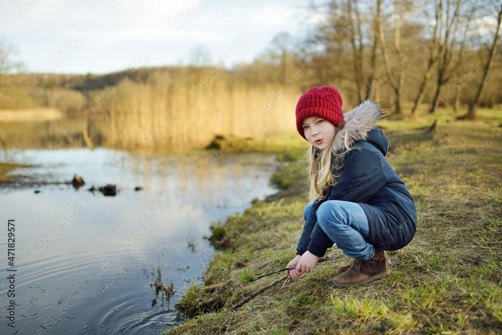 Cute young girl having fun by a river on warm spring day. Child playing by a water. Cute young girl having fun by a river on warm spring day. Child playing by a water.