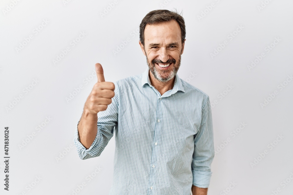 Middle age hispanic man with beard standing over isolated background doing happy thumbs up gesture with hand. approving expression looking at the camera showing success. Middle age hispanic man with beard standing over isolated background doing happy thumbs up gesture with hand. approving expression looking at the camera showing success.