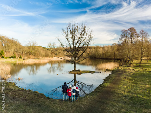 Aerial view of family of four having fun by a lake or pond on sunny spring day. Family having quality time together outdoors.