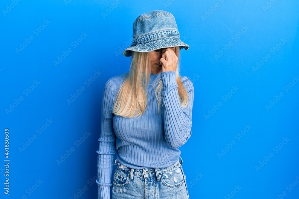 Young blonde woman wearing casual denim hat tired rubbing nose and eyes feeling fatigue and headache. stress and frustration concept.