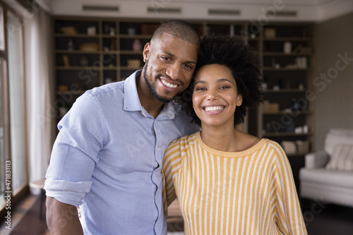 Happy young African American couple home head shot portrait. Millennial spouses standing in own apartment, hugging, looking at camera with toothy smile. Love, marriage, relationship concept