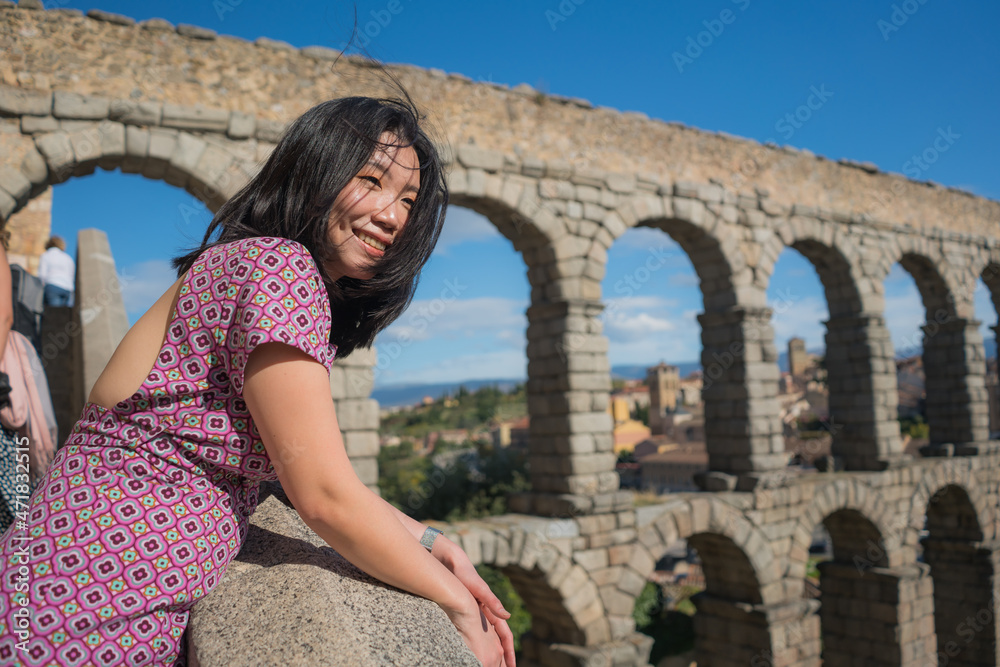 Attractive Asian girl during vacation in Spain - young happy and beautiful Chinese woman visiting world heritage aqueduct in Segovia enjoying holidays travel