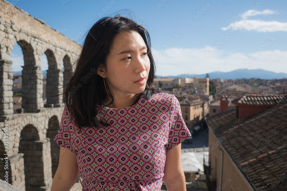 Attractive Asian girl during vacation in Spain - young happy and beautiful Japanese woman visiting world heritage aqueduct in Segovia enjoying holidays travel