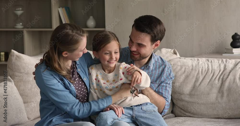 Vídeo do Stock: Overjoyed little girl cuddling with laughing mother father on sofa hold keys from new rented purchased apartment in hand. Excited family young parents preteen daughter get mortgage loan to buy a flat | Adobe Stock 