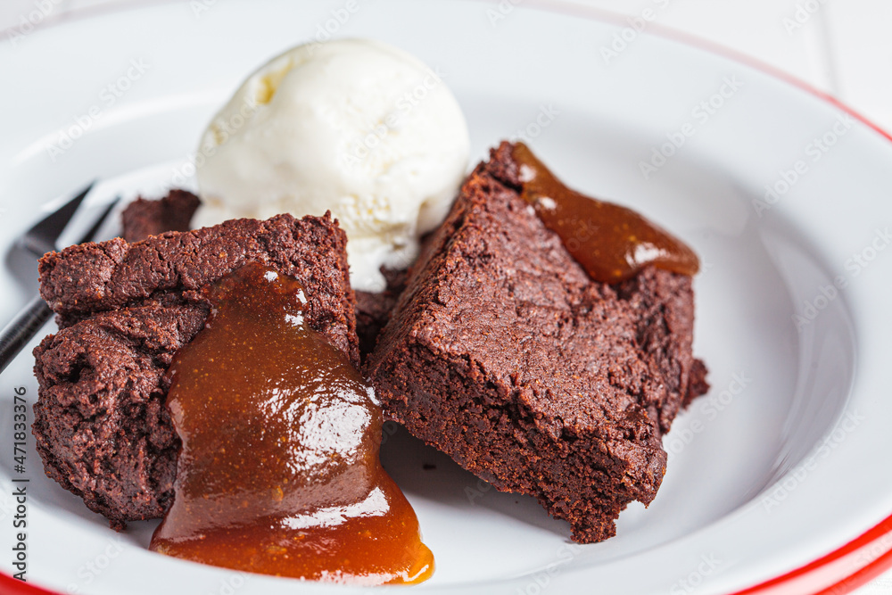 Vegan brownie squares with a scoop of dairy-free ice cream and apple caramel in white plate. Vegan brownie squares with a scoop of dairy-free ice cream and apple caramel in white plate.