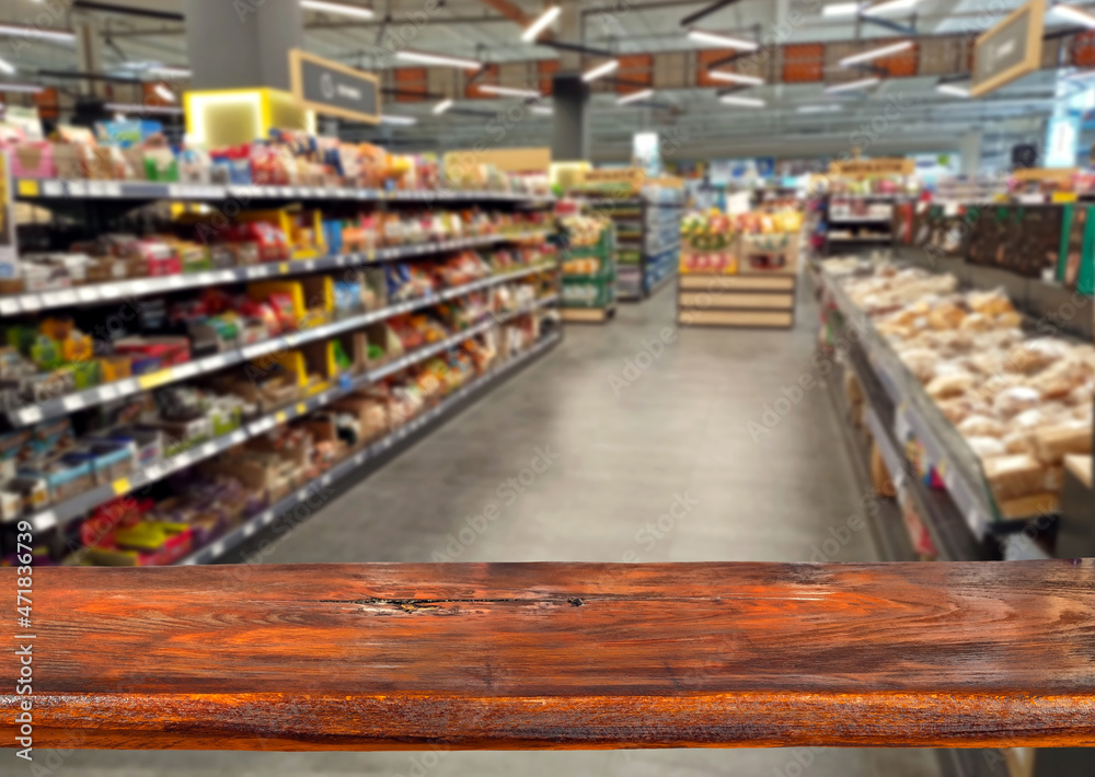 Wooden board on a background of blurred rows with products. Grocery store. Sharpness on the board. Place for product advertising. Free space for design and goods. Layout for products.
