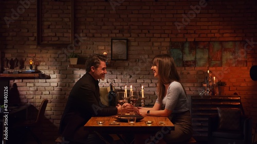 Elegant couple having romantic dinner at home  sitting at table in living room drinking red wine  talking. Stay at home concept.