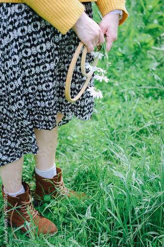 A girl is standing on the grass in old vintage brown shoes. Light vibes, she is relaxed and loves life.
Holds creative tools, a hoop and chamomile flowers. Style cottagecore.