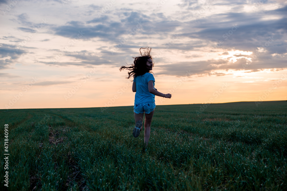 silhouette of a girl running in a field against a sunset background