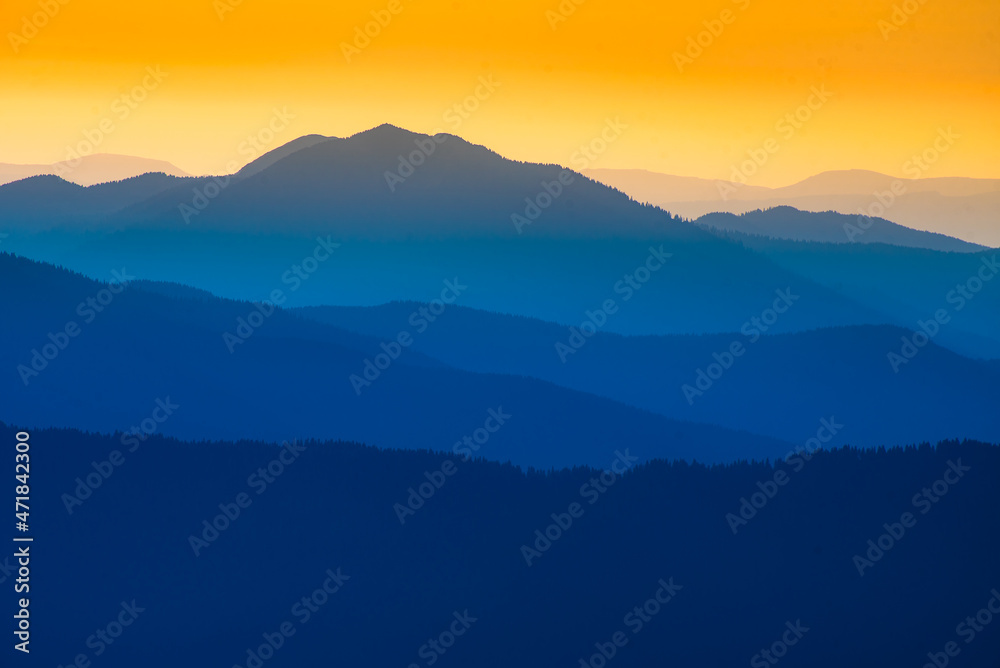  Landscape with blue silhouettes of mountains and hills with beautiful orange  sky. Huge mountain range silhouettes in twilight. 