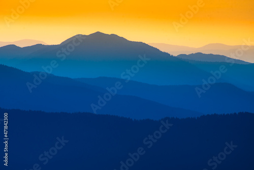  Landscape with blue silhouettes of mountains and hills with beautiful orange sky. Huge mountain range silhouettes in twilight. 