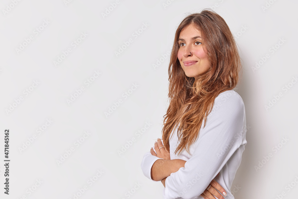 Dreamy thoughtful young woman stands with arms crossed smiles gently dressed in casual jumper concentrated into distance isolated over white background copy space for your promotional content Dreamy thoughtful young woman stands with arms crossed smiles gently dressed in casual jumper concentrated into distance isolated over white background copy space for your promotional content