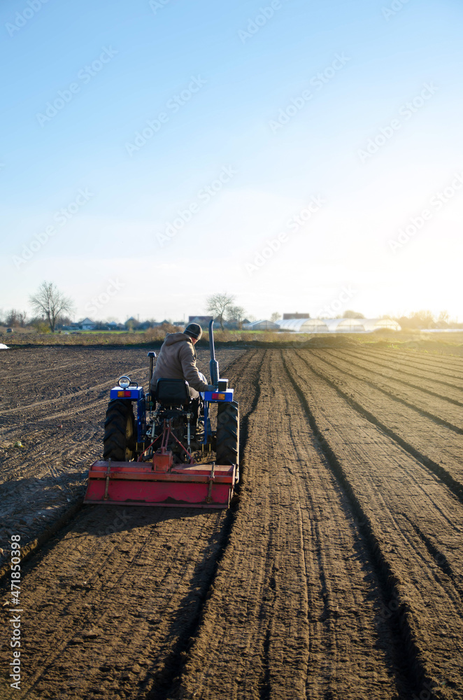 Obraz premium The tractor is cultivating the soil in the farm field. Softening and improving soil qualities. Preparing for cutting rows for the next sowing season in the spring. Farming.