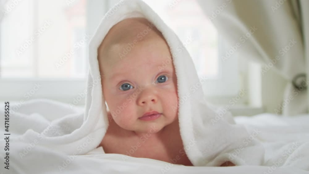 Cute newborn baby is lying on his stomach on the bed wrapped in a white blanket, the newborn is drying in a towel after taking a bath. Concept of child development. Cute newborn baby is lying on his stomach on the bed wrapped in a white blanket, the newborn is drying in a towel after taking a bath. Concept of child development.
