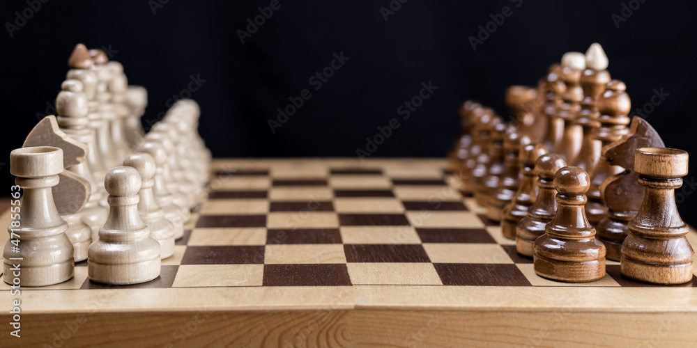 Chess, the beginning of the game. Chess pieces on a wooden chessboard. Advertising on a banner. Chess, the beginning of the game. Chess pieces on a wooden chessboard. Advertising on a banner.