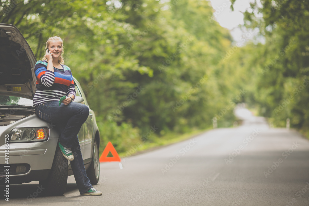 Pretty, young woman with her car broken down by the roadside, setting up the safety triangle, waiting for assistance Pretty, young woman with her car broken down by the roadside, setting up the safety triangle, waiting for assistance