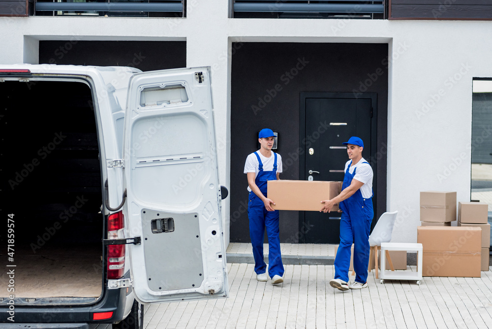 Two removal company workers are loading boxes and furniture into a minibus.