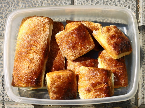 Puff pastry buns close-up in a plastic container on the concrete tiles of the path in summer