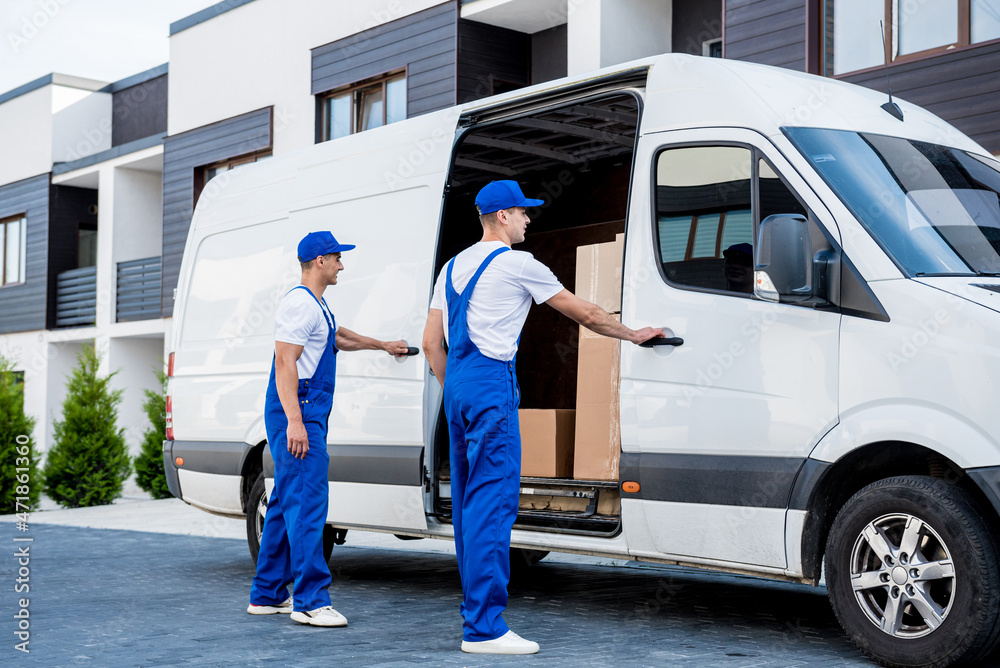 Two removal company workers are loading boxes into a minibus. Two removal company workers are loading boxes into a minibus.