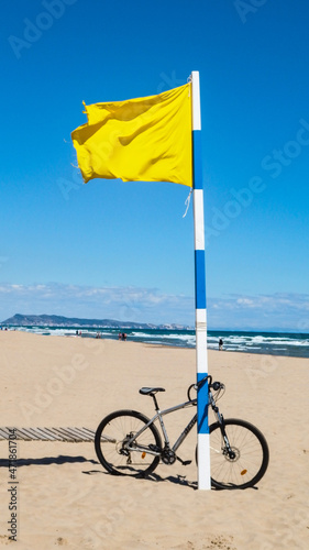 Bandera amarilla ondeando al viento en la playa con bicicleta a poyada en el mástil photo