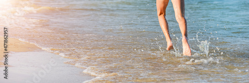 Running girl legs on the sea beach. Long summer banner with copy space. Close up of a young girl's legs walking or running on the beach with waves and seafoam.