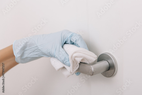 Cleaning black door handles with an antiseptic wet wipe in blue gloves. Sanitize surfaces prevention in hospital and public spaces against corona virus. Woman hand using towel for cleaning