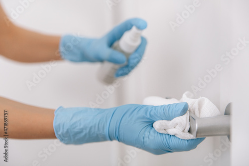 Cleaning black door handle with an antiseptic wet wipe, blue gloves and sanitizer. Woman hand using towel for cleaning. Sanitize surfaces prevention in hospital and public spaces against corona virus