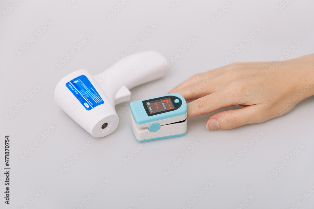 Pulse oximeter and thermometer gun on white background. Measuring oxygen saturation, pulse rate and oxygen levels. Infrared isometric thermometer gun to check body temperature for virus symptoms Pulse oximeter and thermometer gun on white background. Measuring oxygen saturation, pulse rate and oxygen levels. Infrared isometric thermometer gun to check body temperature for virus symptoms