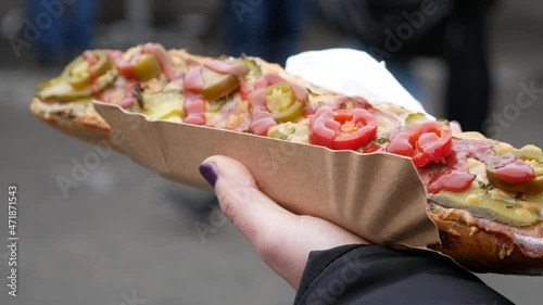 Female hand holding delicious sandwich called Zapiekanka, near Okrąglak street food court on Plac Nowy (Jewish Square). Kazimierz district of Old Town Kraków, famous Zapiekanki Krakowskie.