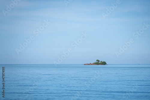 A small island in far distance on the ocean and horizontal line with clearly blue sky. Seascape nature outdoor photo scene.