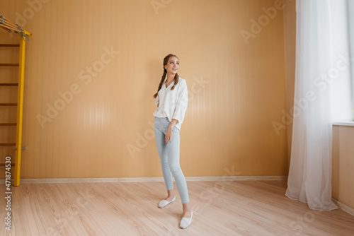 A young woman stands after moving into a new apartment against a wall. Purchase of real estate. Housewarming, delivery and transportation of goods.