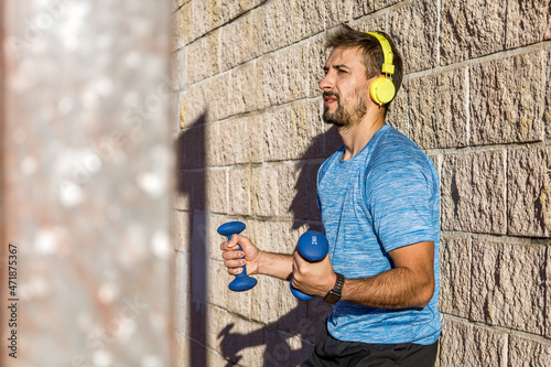 millennial caucasian man with dumbbells in his hands against wall.